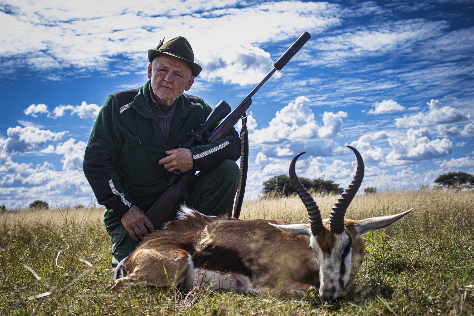 Hunter kneeling with a springbok under dramatic clouds